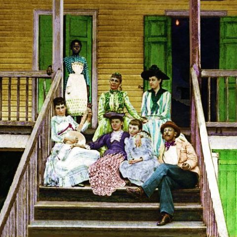 A white family sitting on the steps of a plantation with a slave girl standing behind them