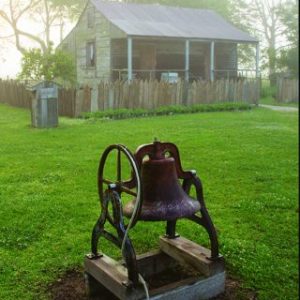 A large bell next to a slave cabin